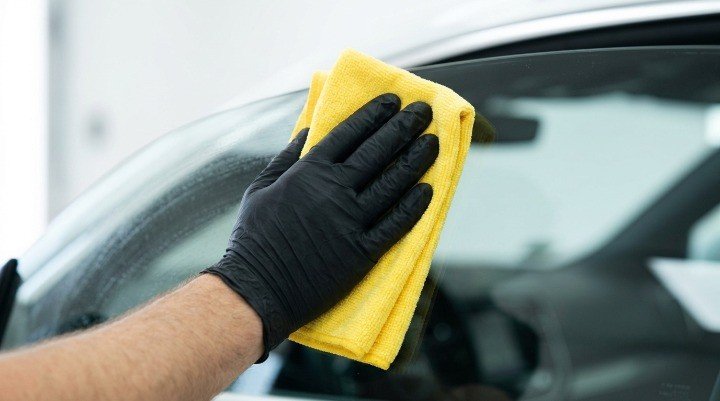 A close-up shot showing a hand using a microfiber cloth to clean a car window without streaks