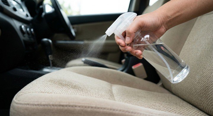 spraying cleaning solution on cloth car seat to remove stains