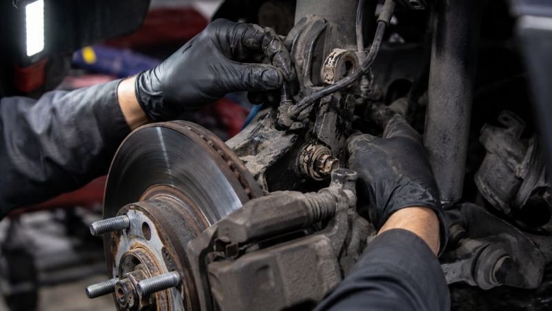 Mechanic inspecting a dirty wheel speed sensor behind a Honda brake rotor