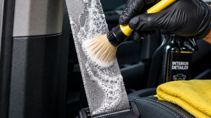 agitating foam cleaner on car seat belt webbing with a soft detailing brush
